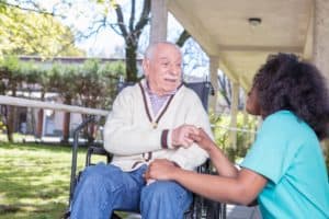 Nurse helping elder patient in hospital garden.